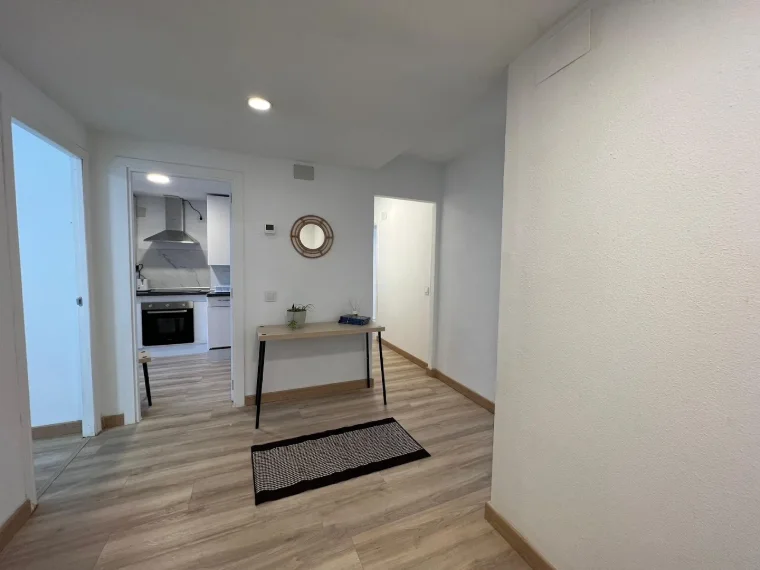 Recibidor de un piso tras una reforma integral, con suelo laminado de madera y paredes blancas